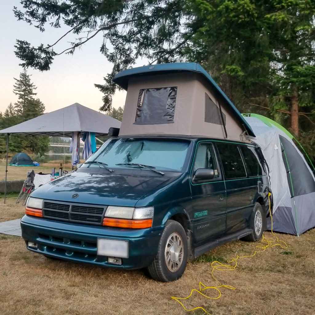 A view of a blue camper van with a tent on top