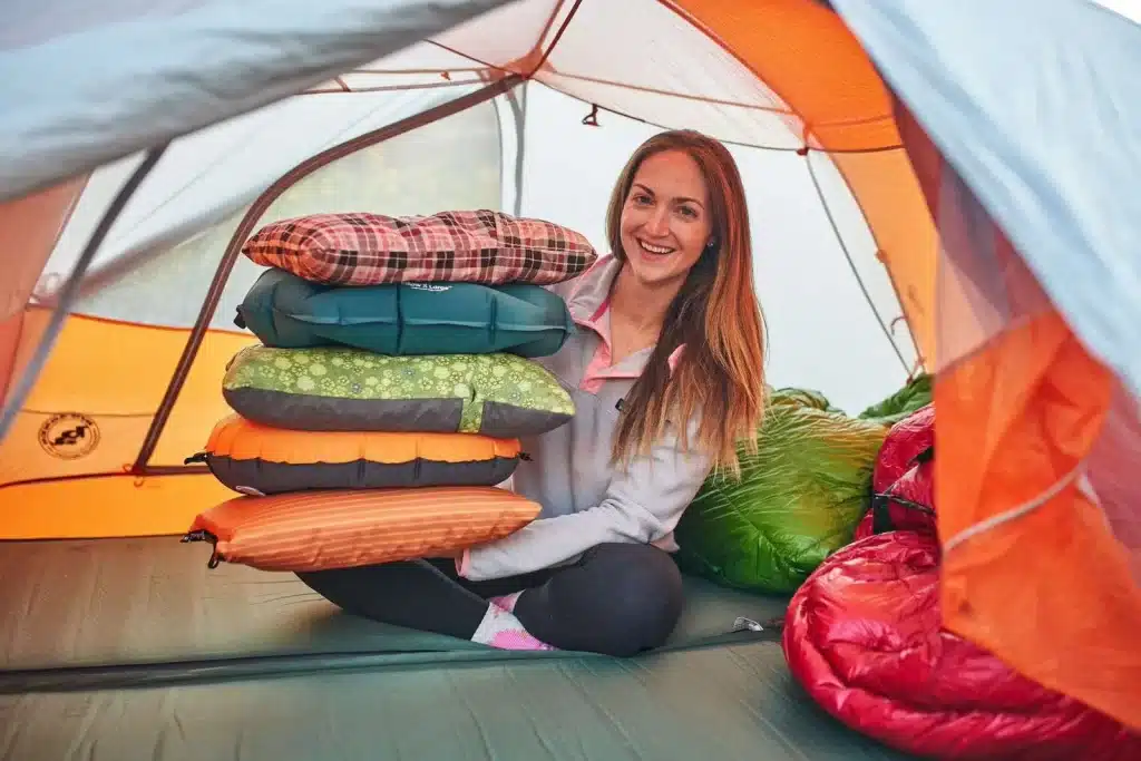 A view of a girl holding a pile of pillows sitting inside a camping tent