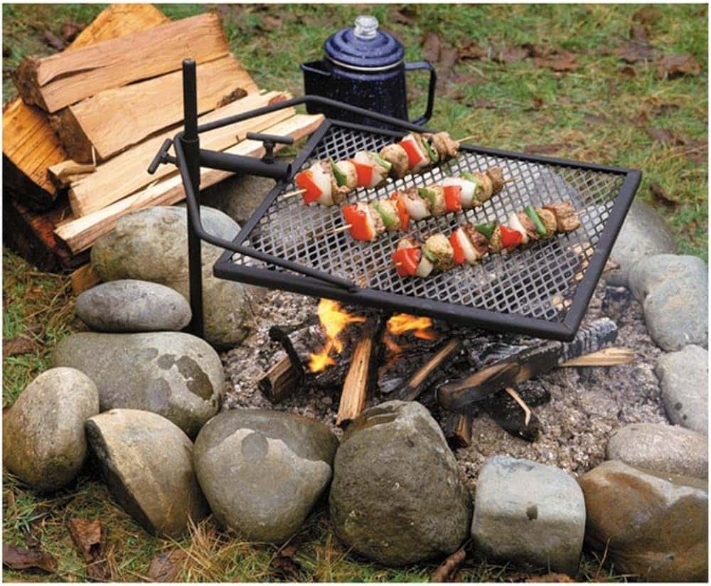 A view of a grill with chicken on skewers under a fire and stones at a camp site