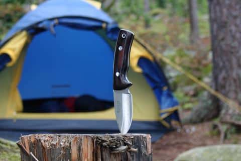 A view of a knife stuck inside a wooden log beside a camping tent