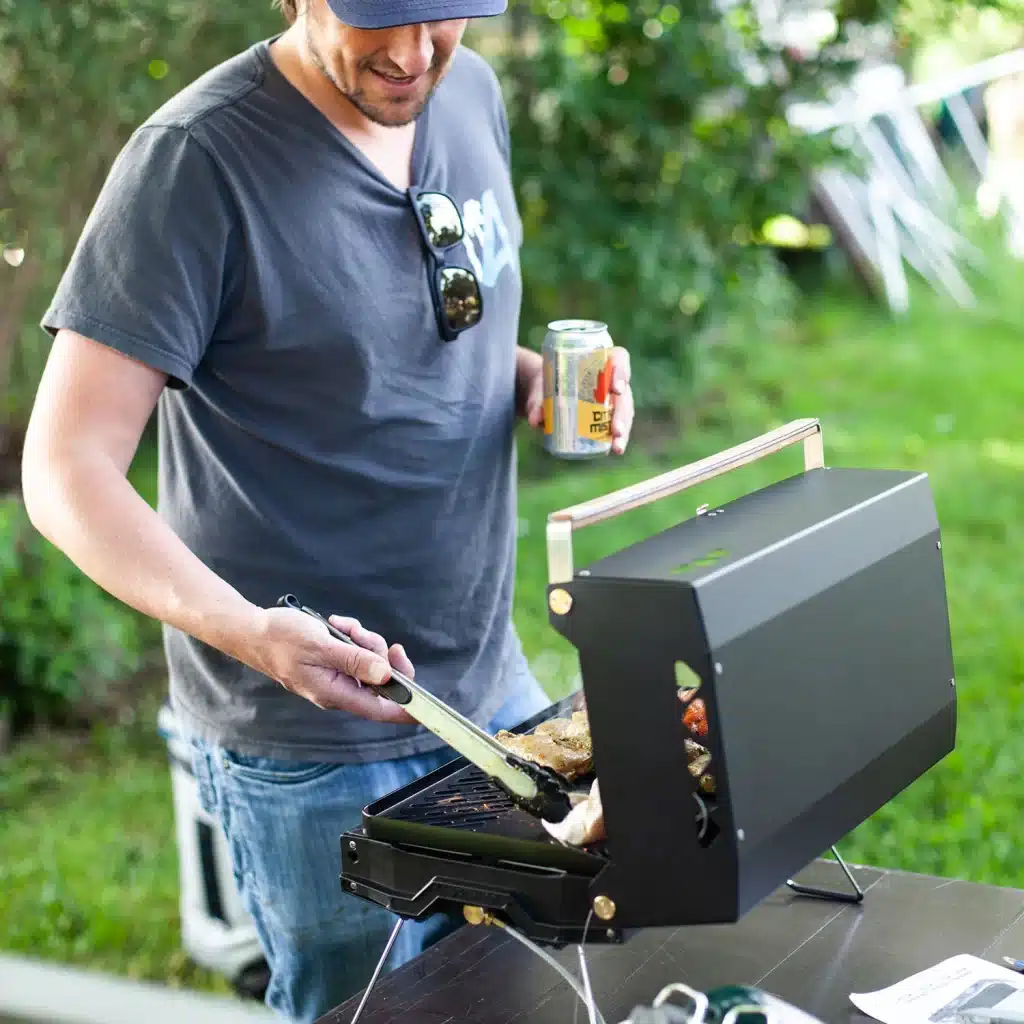 A view of a person checking steak on a grill holding a can of beer