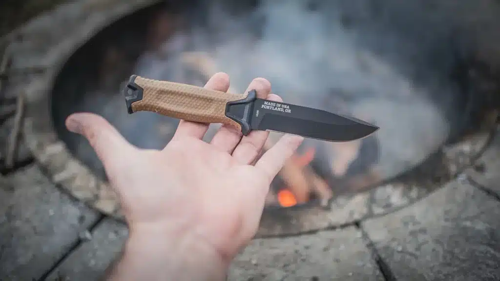 A view of a person holding a knife in hand next to a campfire