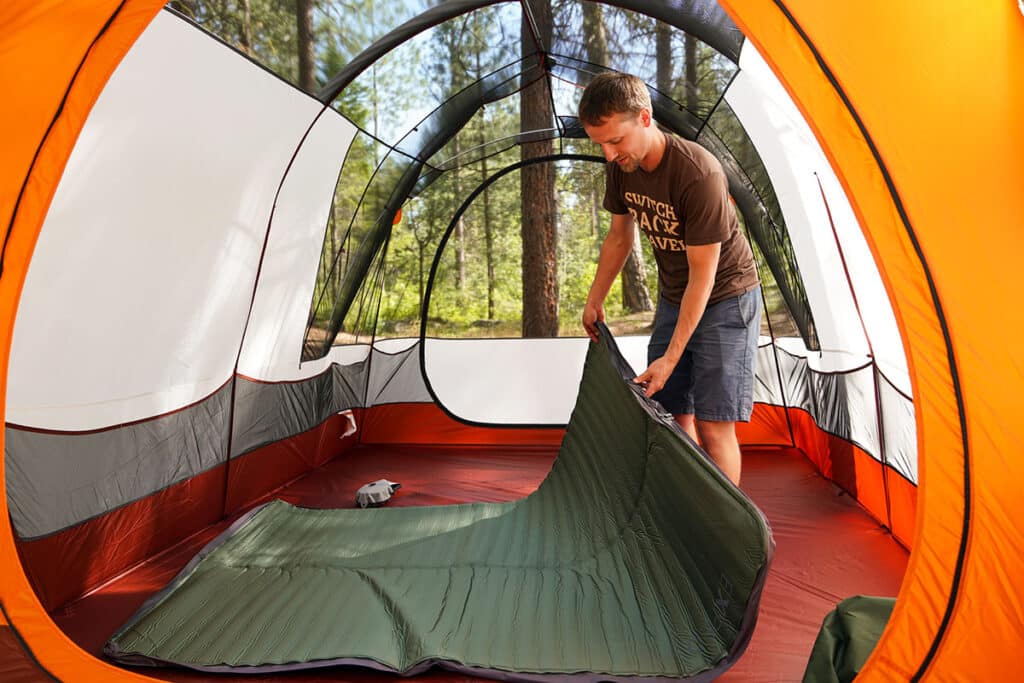 A view of a person setting up an Exped Mega Mat Duo Air Mattress inside a camp