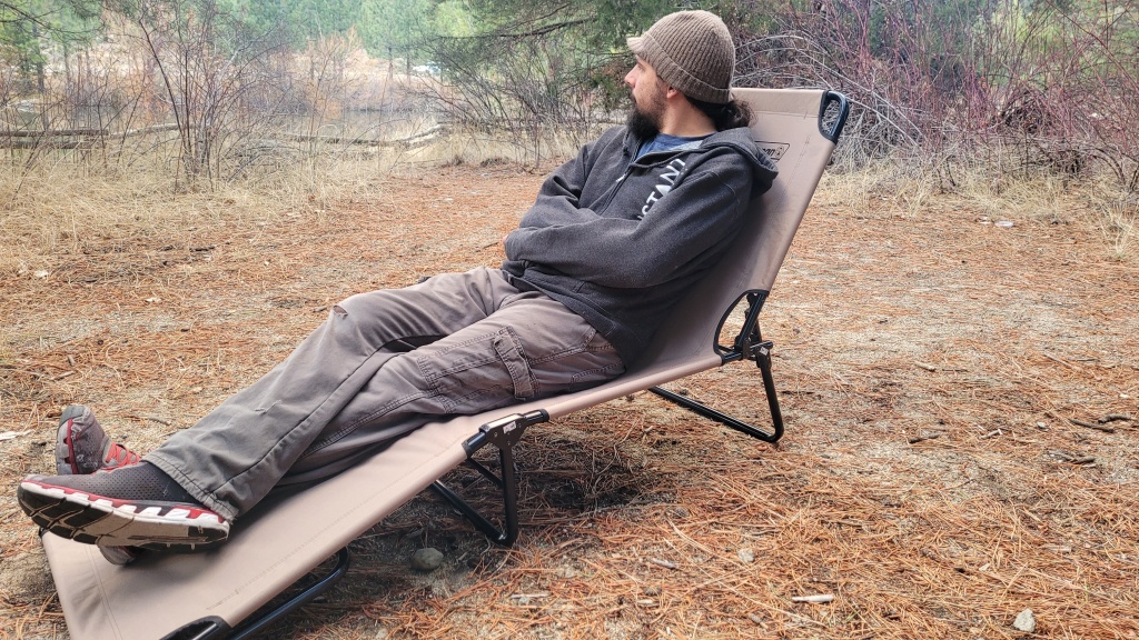 A view of a person sitting on a camping cot in a grassy field