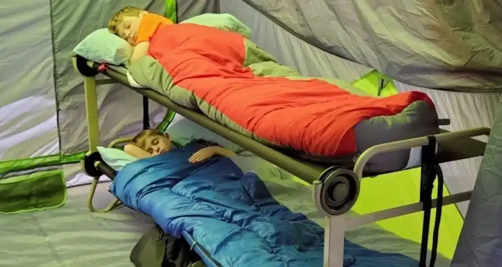 A view of two boys sleeping inside a double decker camping cot