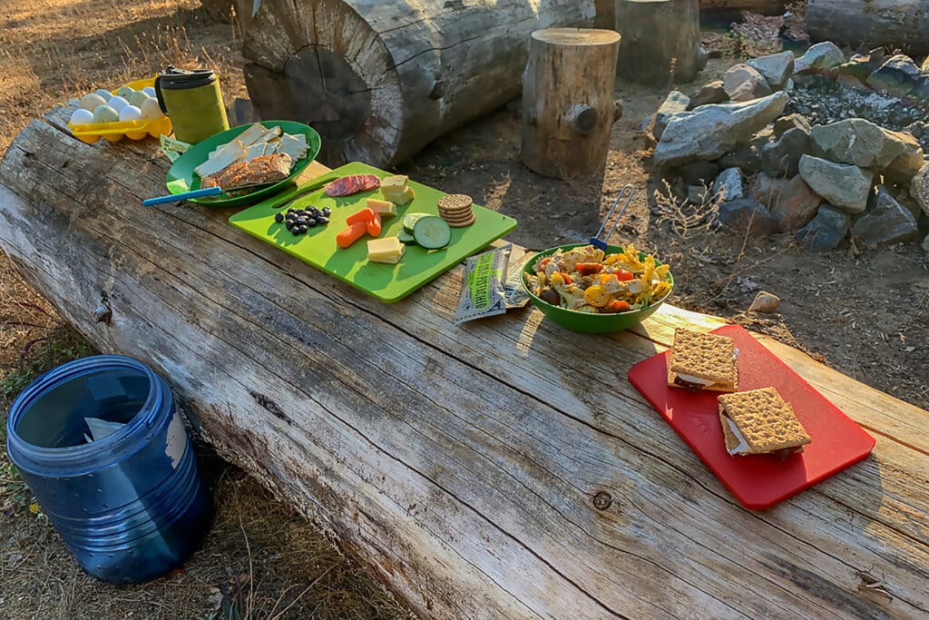 A view of various camping meals placed on a wooden log at a campsite