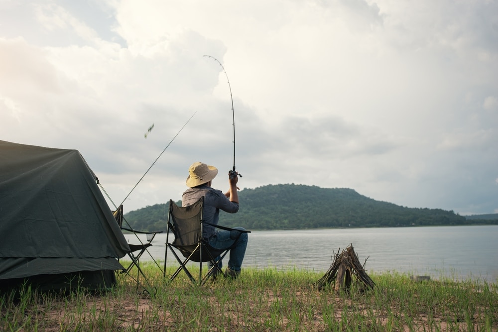 Fisherman with camping tent and bonfire for cooking on the shore of the lake. 