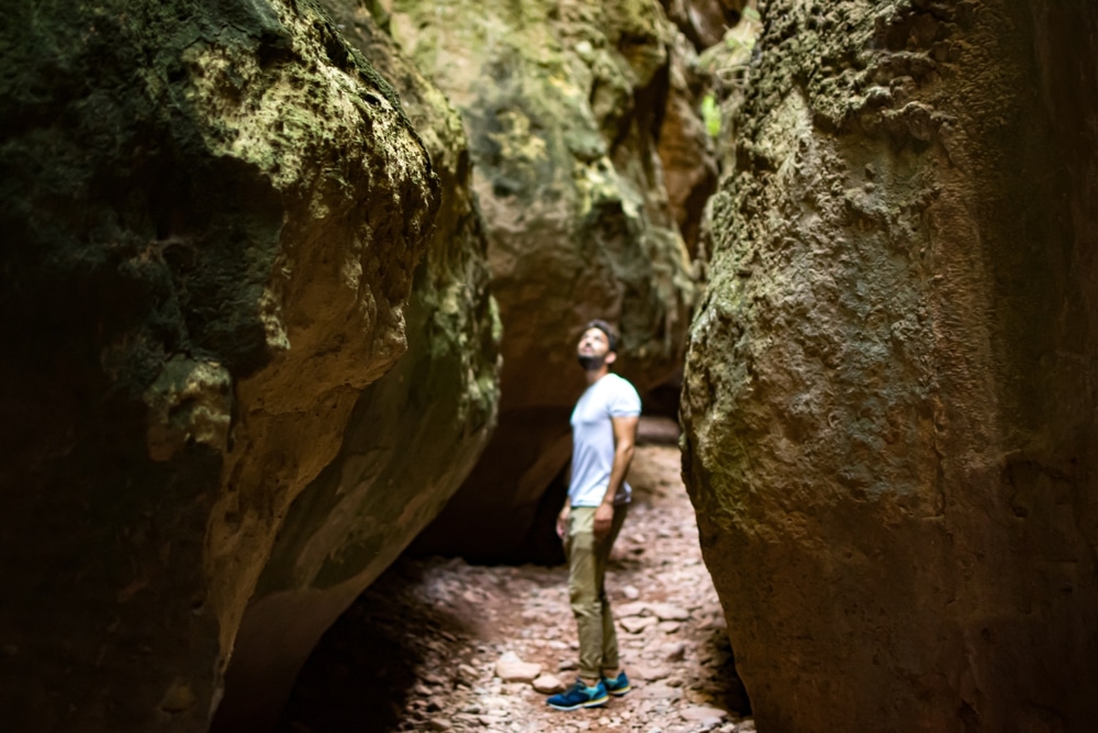  Young man explorer walks through a narrow path in caves 