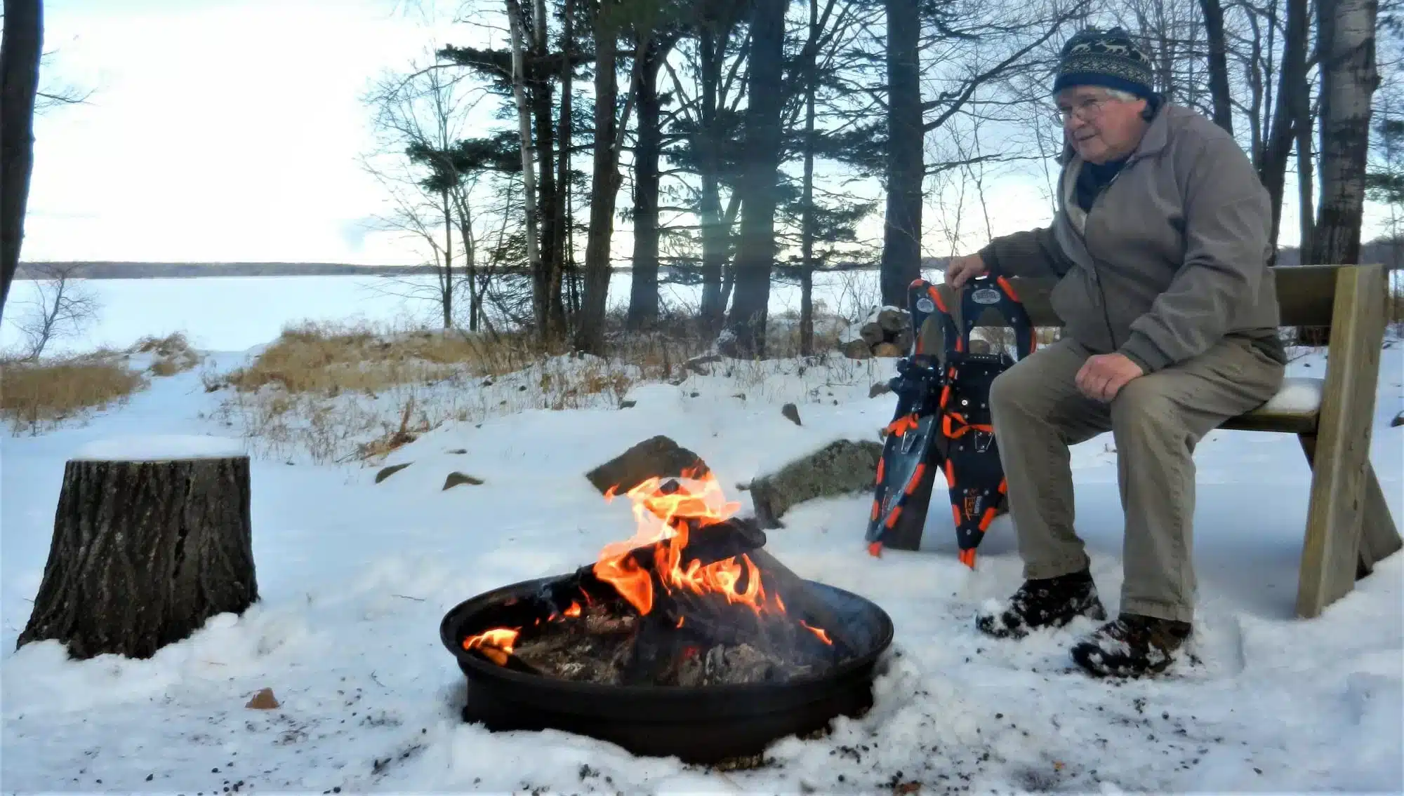 an old man sitting near campfire in snow