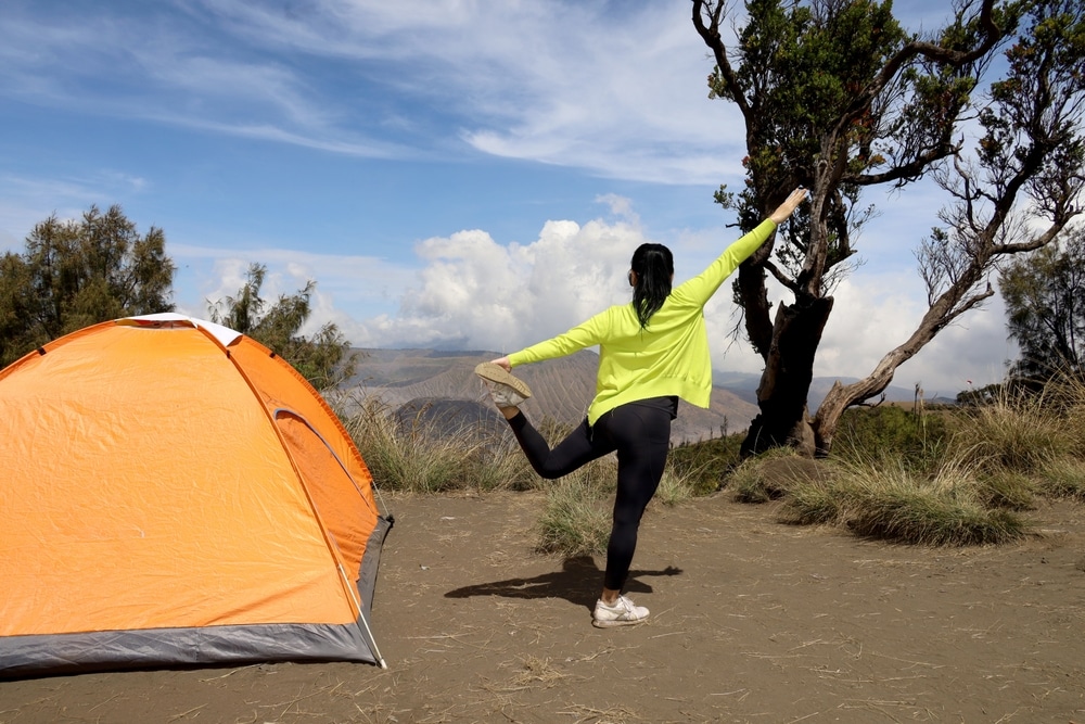 back view of woman doing yoga movements next to her tent while camping at the top of Mount Bromo Indonesia.