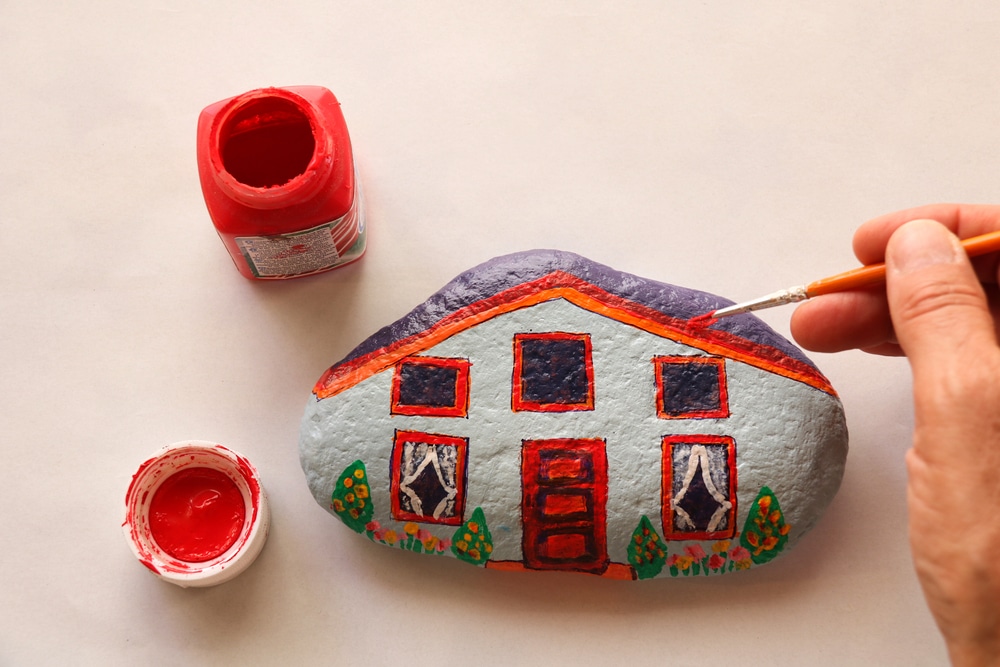 hand with brush painting stone as stylized home