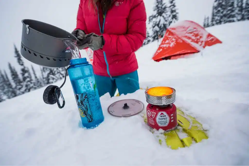 zoomed view of a person puring hot water in bottle in snow