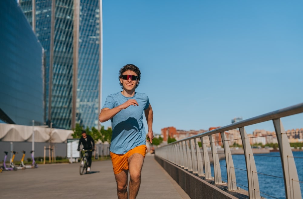 Young Man Running Along A Riverside Pathway Wearing Blue Shirt