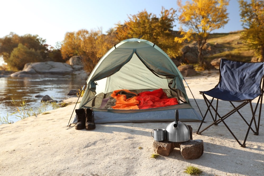 a tent along side water cattle on stones and a camping chair