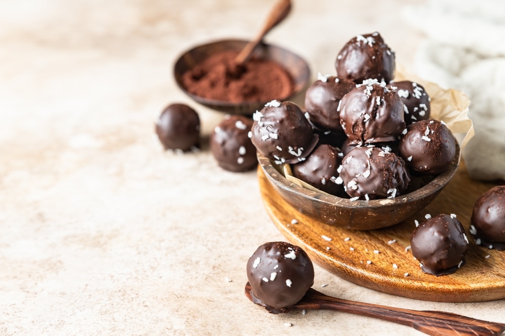 Vegan chickpea and peanut butter candies in chocolate glaze sprinkled with coconut chips 