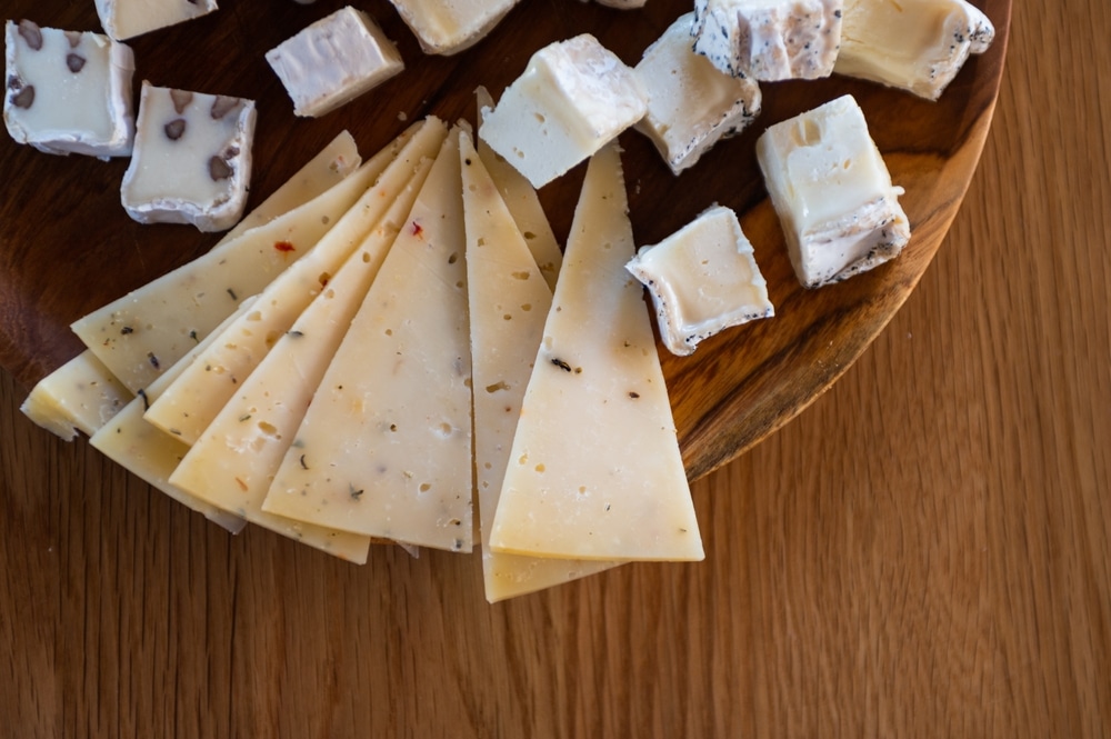 different types of cheese, with mold, hard, with spices, etc. lies on a wooden plate on a wooden table.