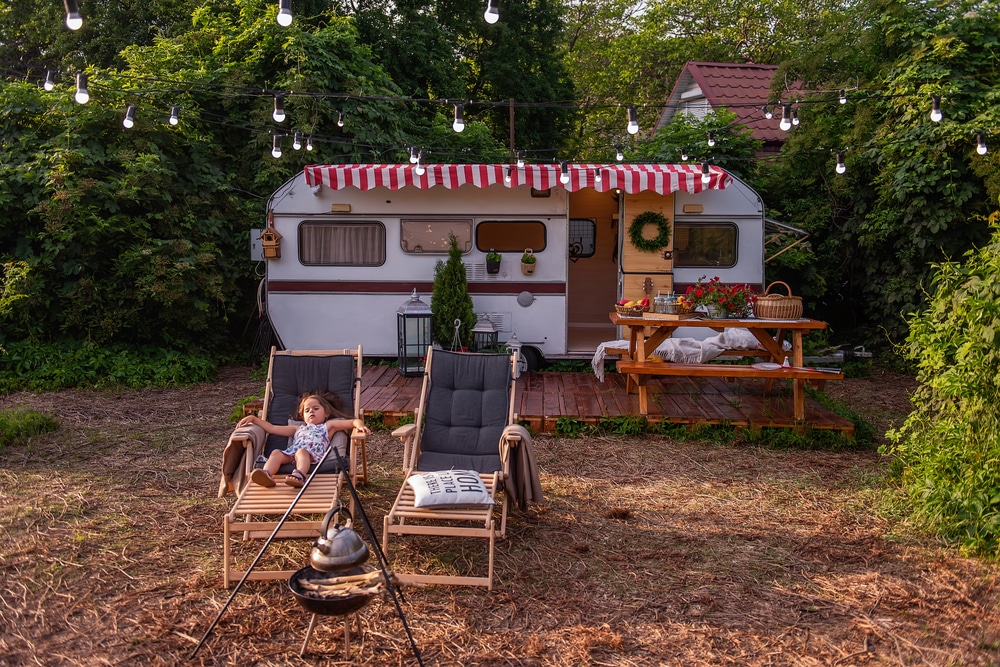 Little girl is resting on wooden deck chair near the trailer track. 